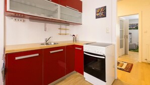 A compact kitchen with red cabinets, a white stove, and a small sink. - Apartment Rudolfspark Check in 15h to 22h Only (Vienna)