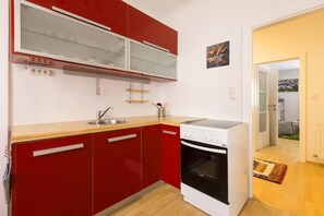 Een compacte keuken met rode kastjes, een witte kookplaat en een klein spoelbakje.