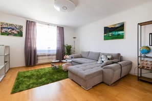 A modern living room with a grey sectional sofa, a green rug, a globe on a shelf, and artwork on the walls.