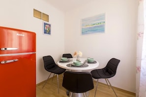 Een eethoek met een ronde tafel, zwarte stoelen en een rode koelkast.