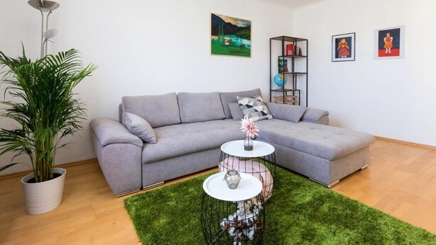A modern living room with a grey sofa, a small round table with a vase, a tall floor lamp, and a bookshelf. - Apartment Rudolfspark Check in 15h to 22h Only (Vienna)