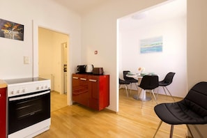 A compact kitchen with a stove, a red cabinet, and a dining area with chairs and a table.