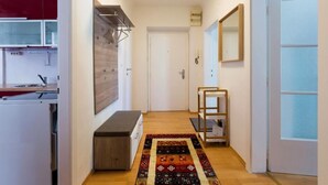 A hallway with a kitchen on the left, a bench, a patterned rug, and a door on the right. - Apartment Rudolfspark Check in 15h to 22h Only (Vienna)