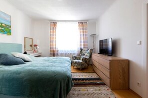 Een slaapkamer met een bed, een televisie, een stoel en een dressoir.