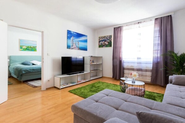 Een moderne woonkamer met een flatscreen televisie, een bank, een salontafel en een groen vloerkleed.