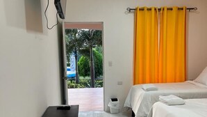 A hotel room with two beds, a TV mounted on the wall, a small black cabinet, and a window with a view of greenery outside. - Hotel Campestre Bella Vista (Moyagalpa)