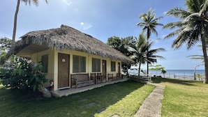 A thatched-roof building with a balcony, surrounded by palm trees and a view of the sea.