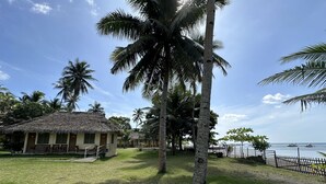 A tropical resort with thatched-roof huts, palm trees, and a view of the sea.