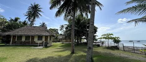 A tropical resort with thatched-roof huts, palm trees, and a view of the sea.