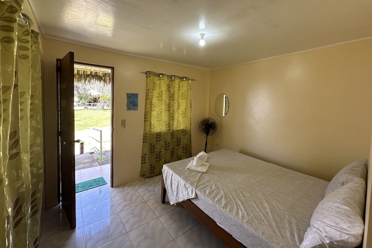 A bedroom with a bed, a ceiling fan, a window with curtains, and a door leading outside.