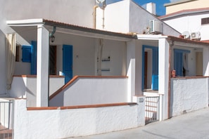 A white building with blue shutters, a covered porch, and a gated entrance.