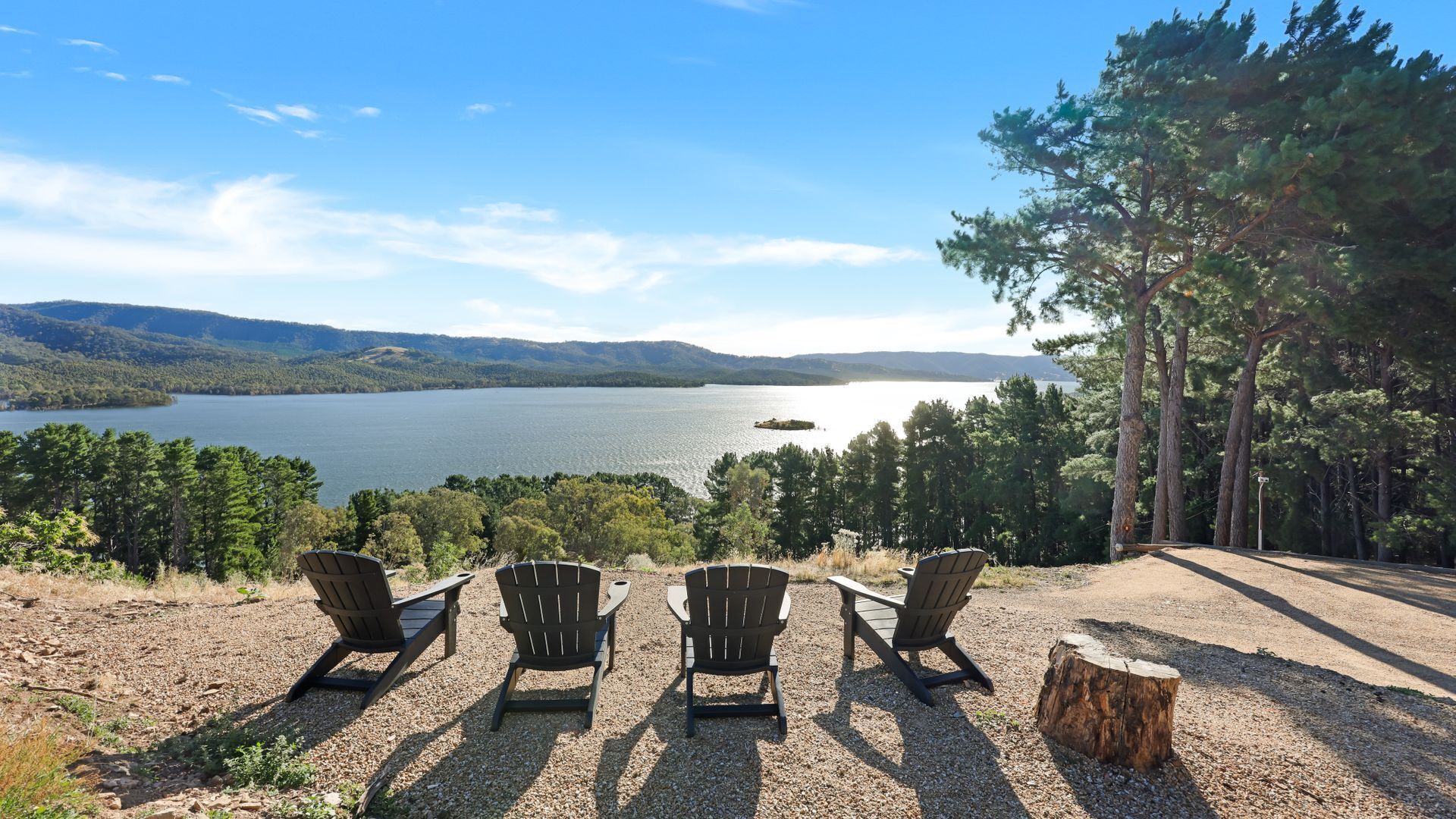 A view of a lake with chairs facing the water, surrounded by trees and hills.
