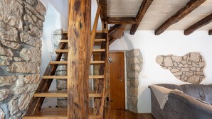 A wooden staircase leading to a door, a stone wall, and a grey sofa in a room with wooden beams and a stone accent wall. - Villa Zaria (Kvarner - Mošćenička Draga) (Mošćenička Draga)