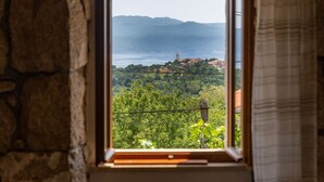 A window view of a coastal landscape with a stone wall, a distant tower, and lush greenery. - Villa Zaria (Kvarner - Mošćenička Draga) (Mošćenička Draga)