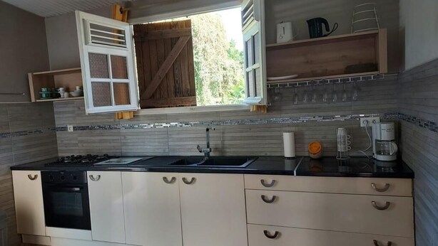 A modern kitchen with a central island, a built-in oven, and a window with open shutters. - Maison ras Campagne (Rivière-Salée)