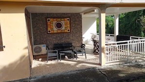 A covered outdoor seating area with a stone wall, a decorative tile, and a white railing. - Maison ras Campagne (Rivière-Salée)