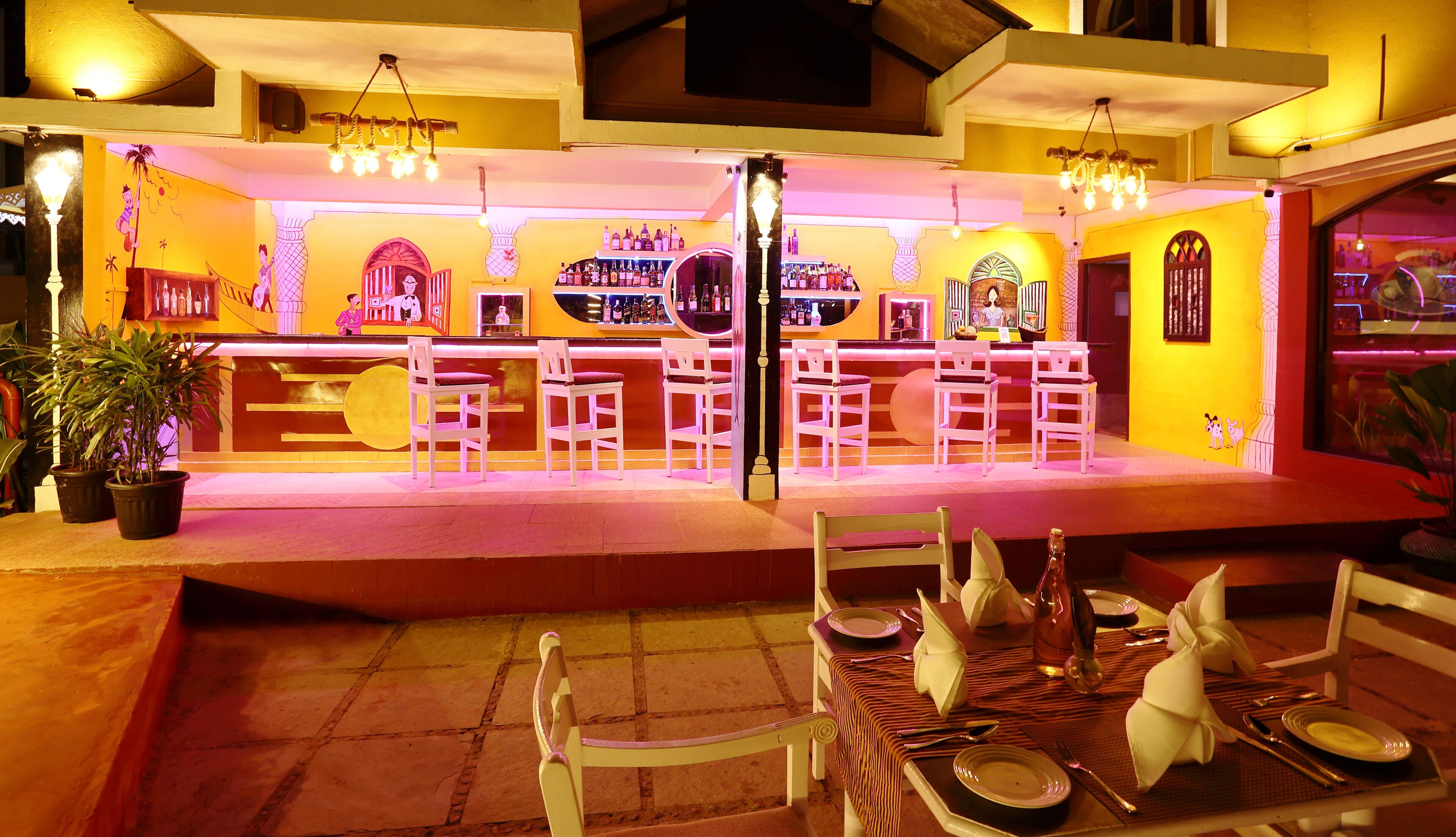 A bar area with white chairs and a counter displaying bottles.