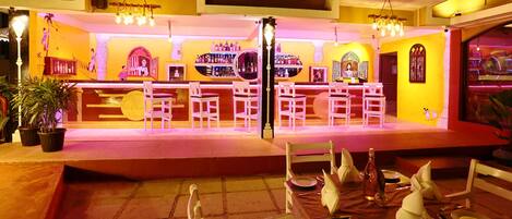 A bar area with white chairs and a counter displaying bottles.