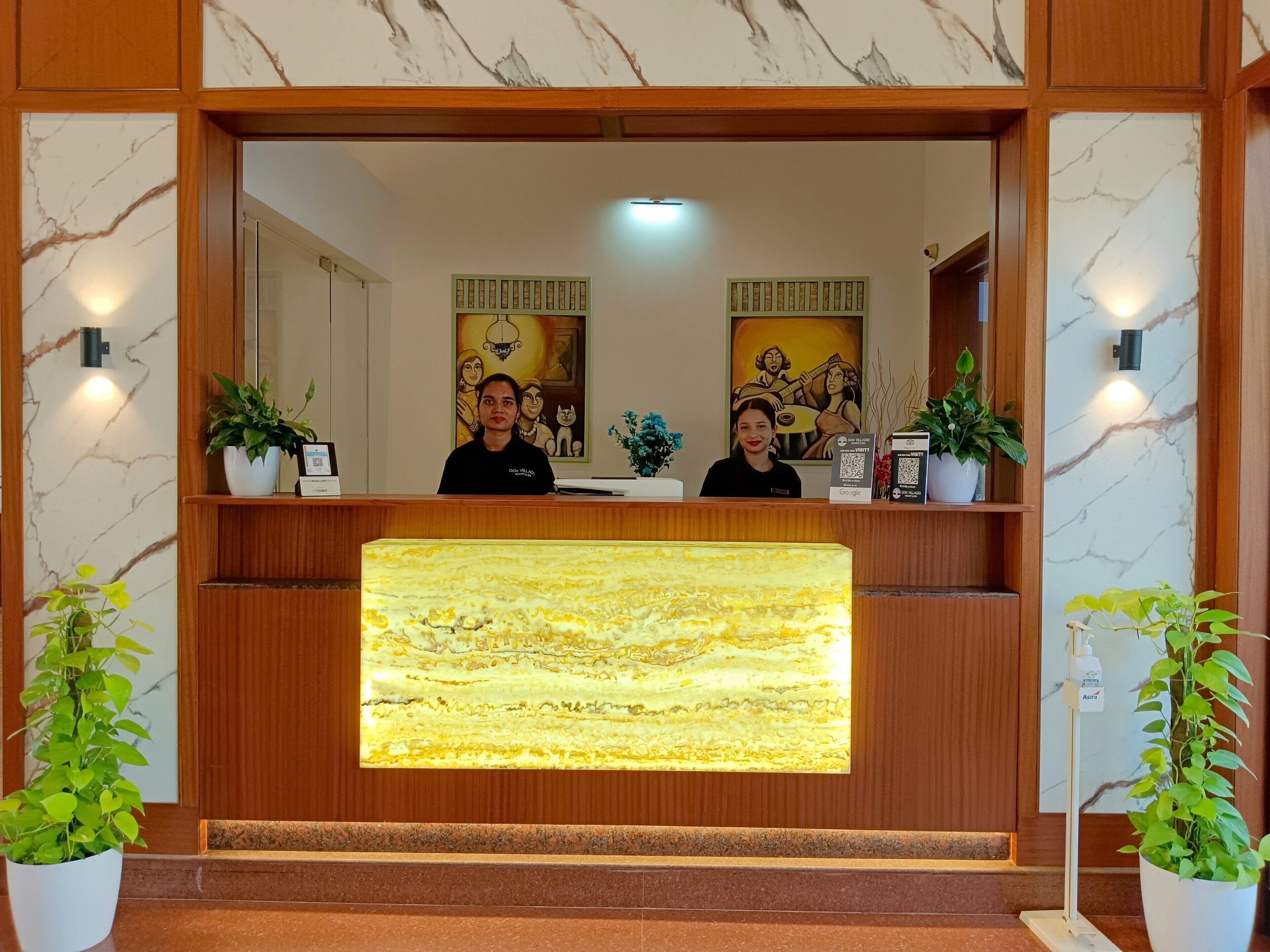A reception desk with a marble-like design, two potted plants, and a large illuminated panel.
