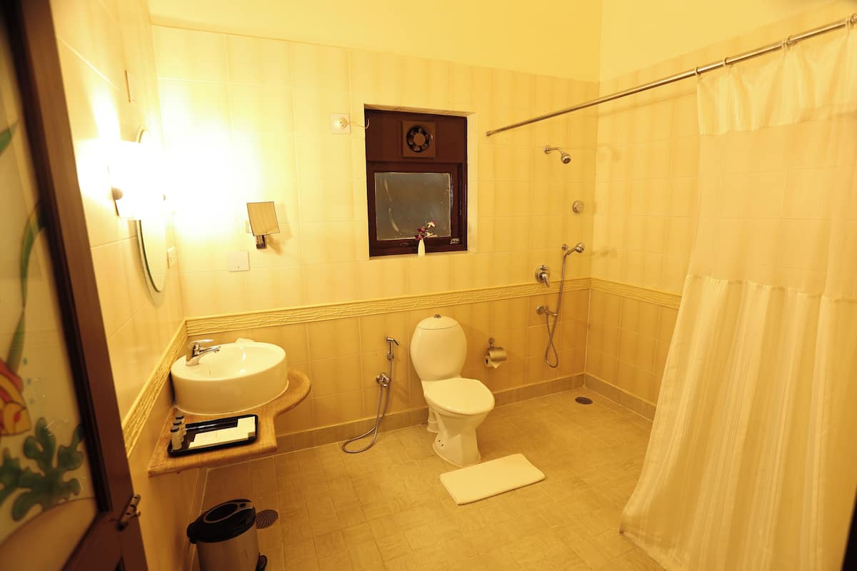 A bathroom with a sink, toilet, shower, and a small window.