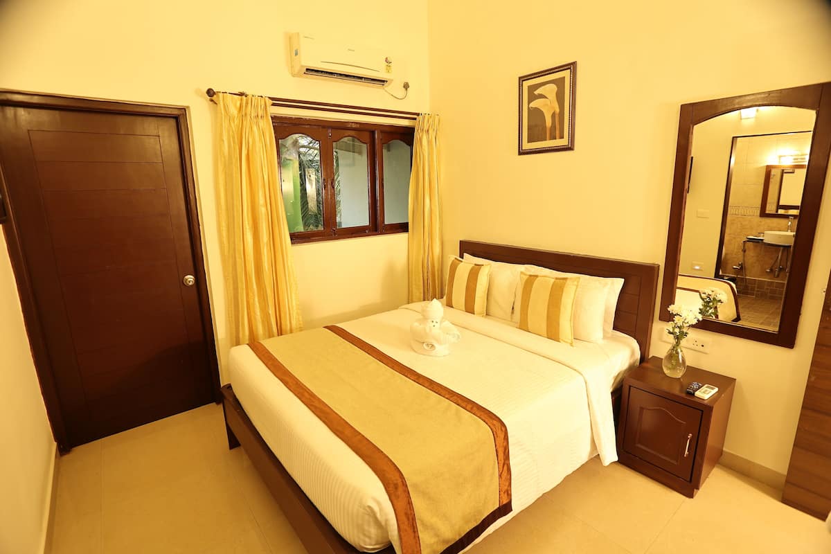 A hotel room with a bed, a nightstand, a mirror, a window with curtains, and an air conditioning unit.