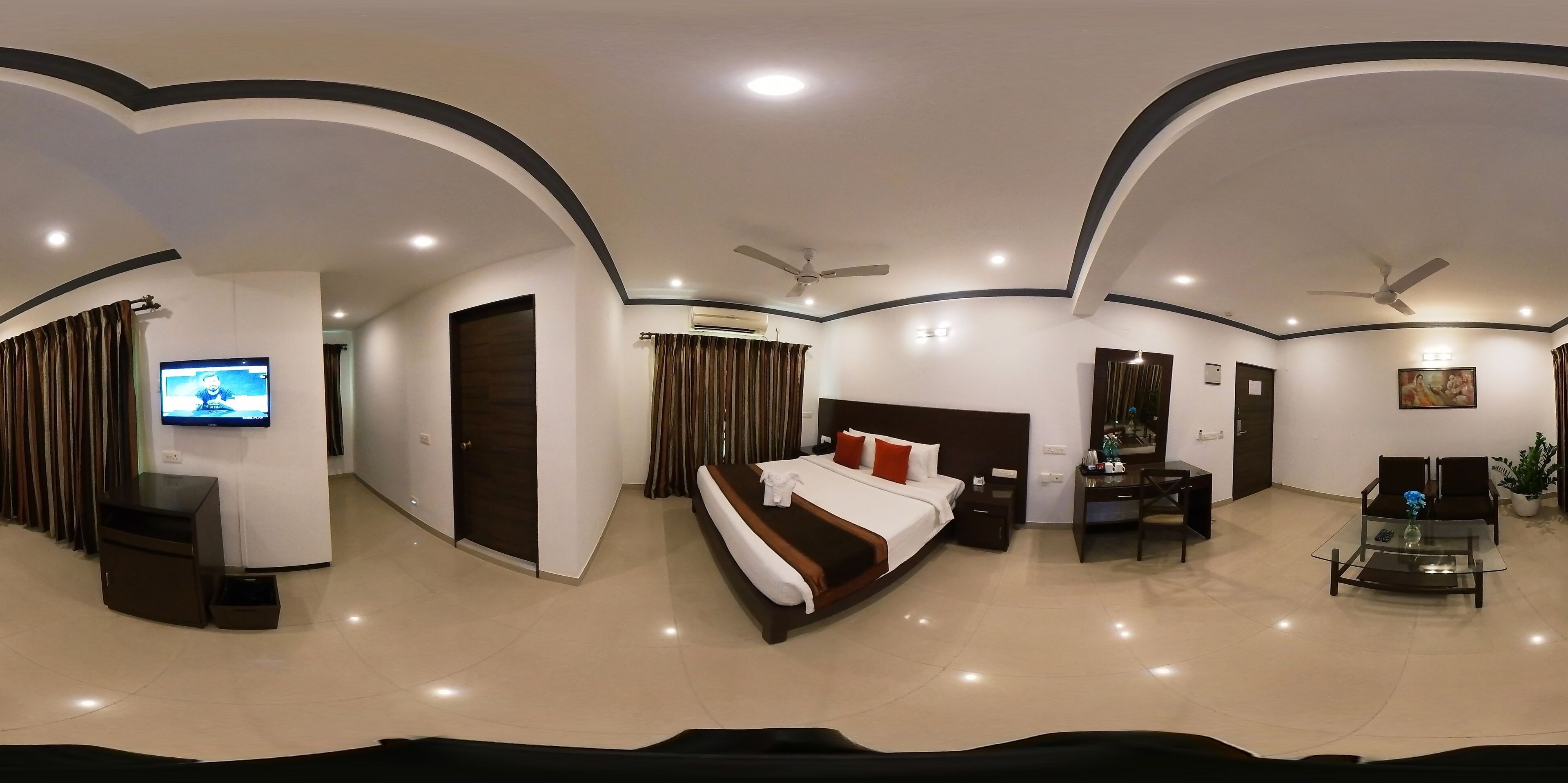 A modern hotel room with a large bed, a desk, a television, and a ceiling fan.