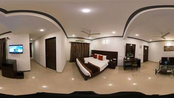 A modern hotel room with a large bed, a desk, a television, and a ceiling fan.
