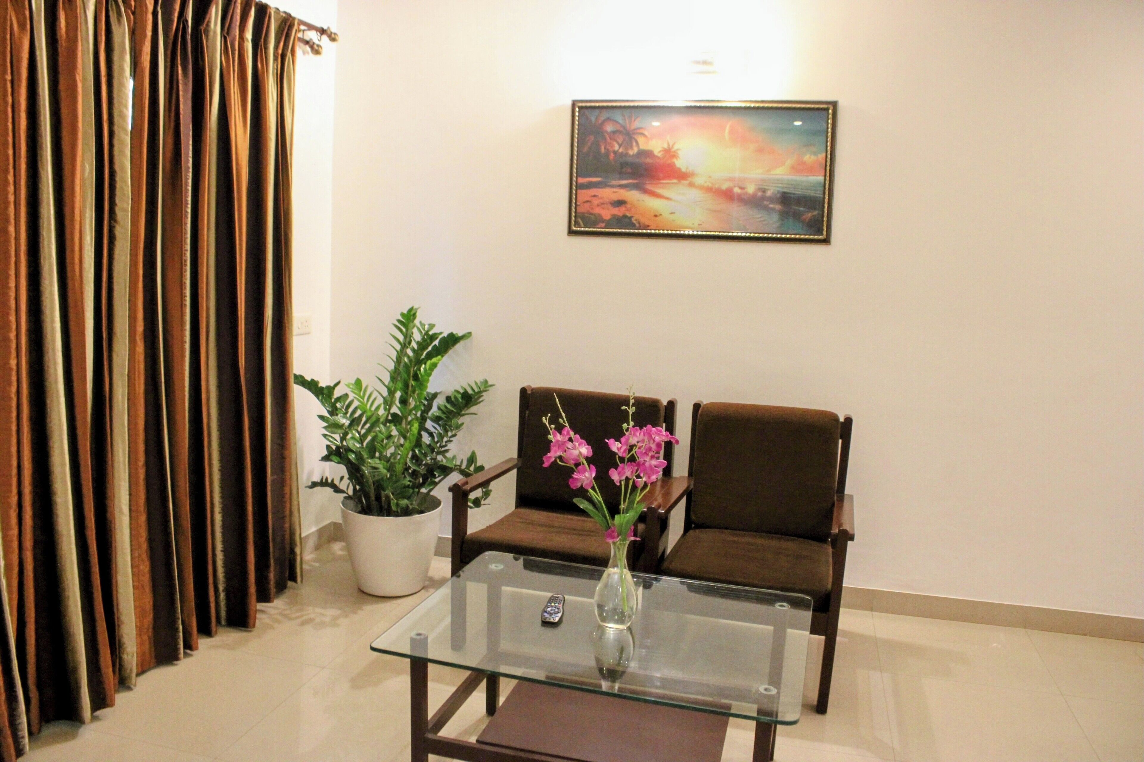 A living room with a glass coffee table, two brown sofas, a potted plant, and a painting on the wall.