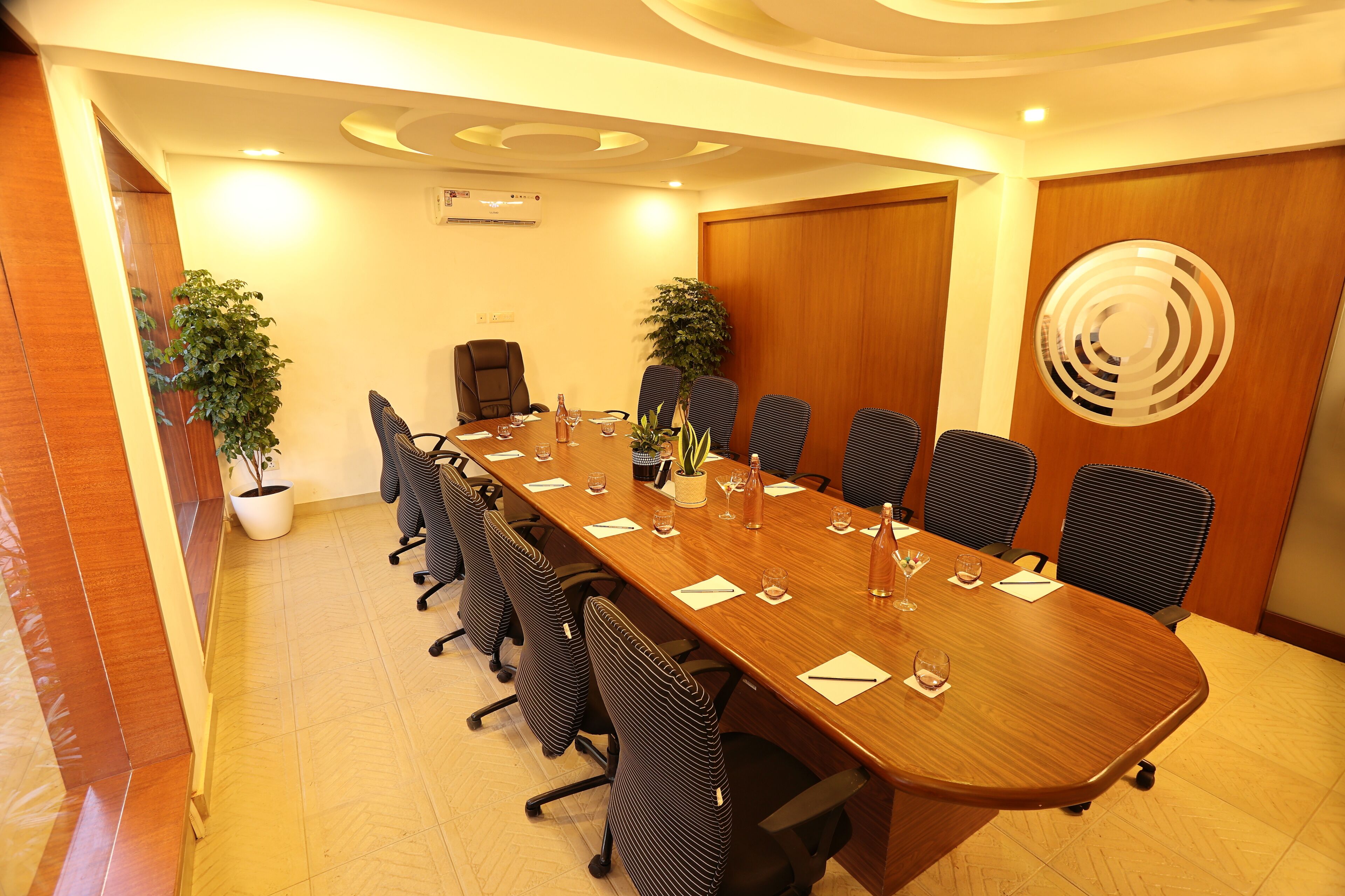 Un salón de conferencias con una larga mesa, sillas, plantas en macetas y una puerta de madera.
