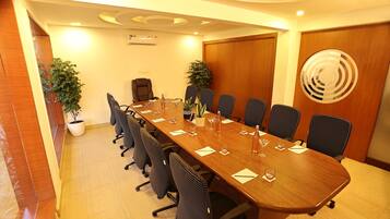 Un salón de conferencias con una larga mesa, sillas, plantas en macetas y una puerta de madera.