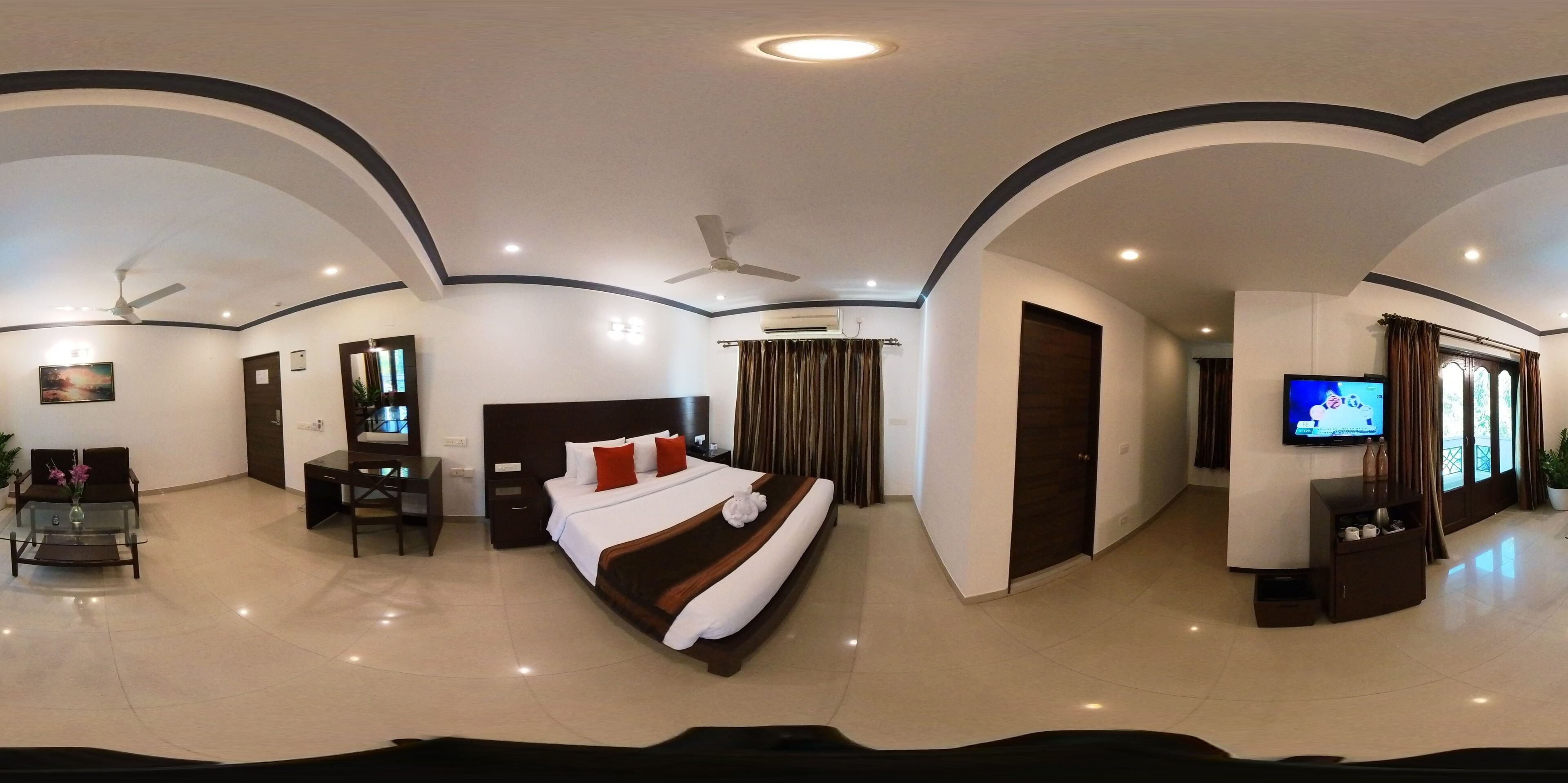 A hotel room with a large bed, a desk, a TV, and a seating area with a table and chairs.