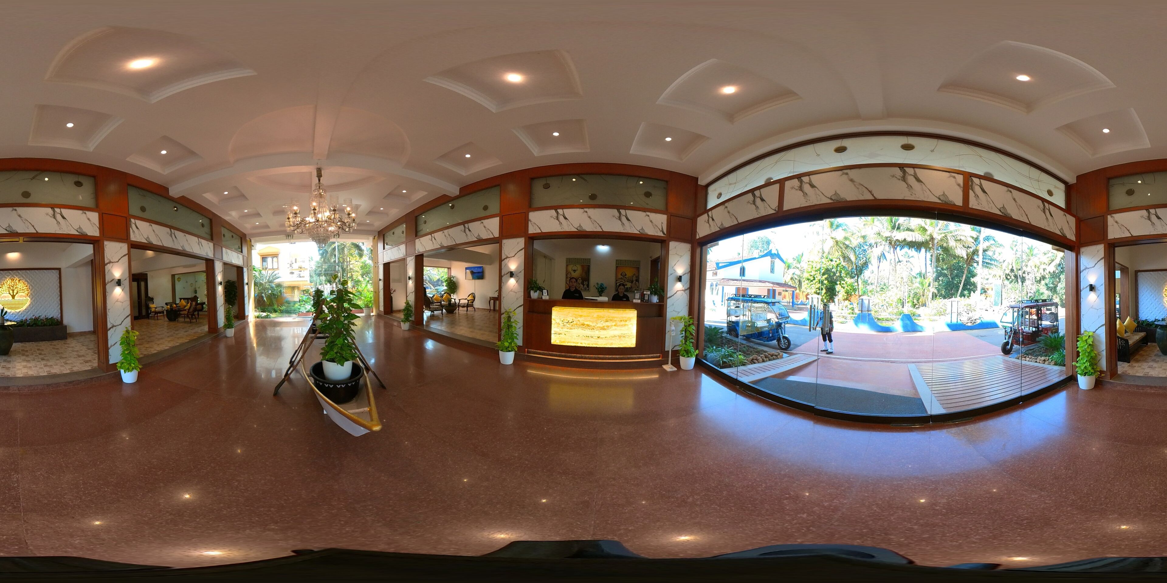 A spacious lobby with a reception desk, potted plants, and a large glass window offering a view of the outside.