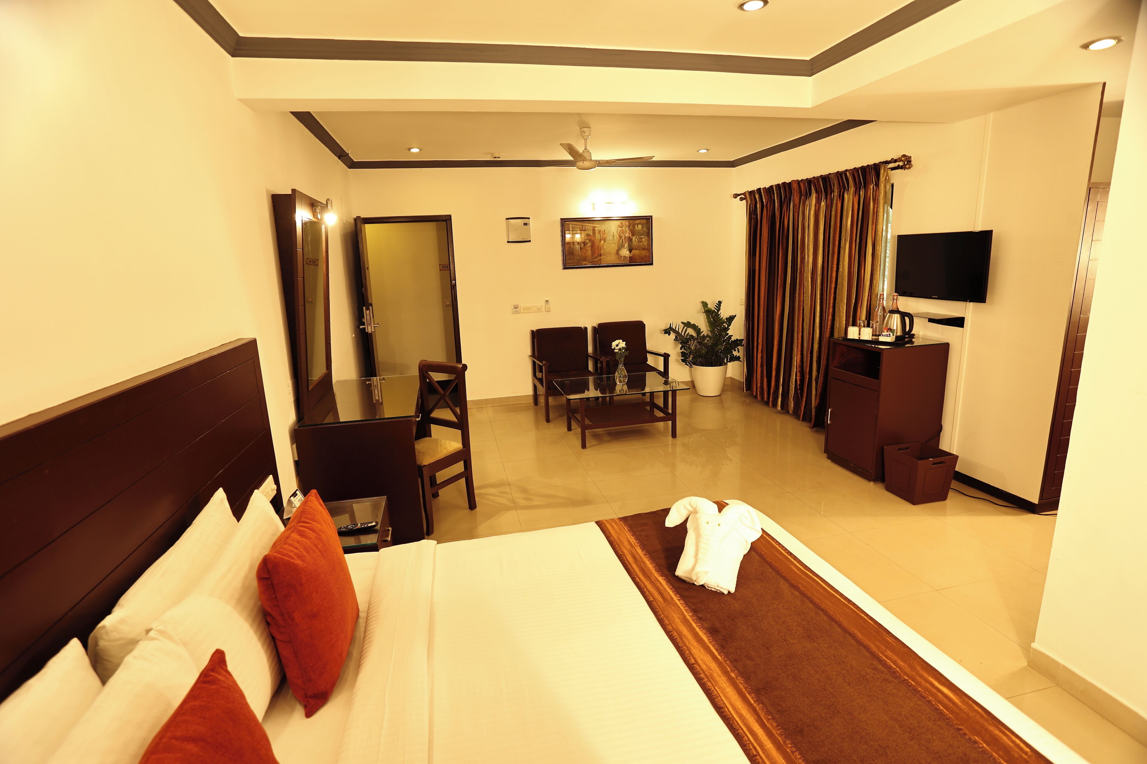 A hotel room with a bed, a desk, a chair, a television, and a plant.