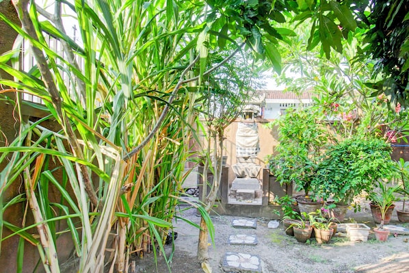 A courtyard with a stone pathway, potted plants, and a statue. - OYO Life 93284 Kos Cendana Raya (Mataram)