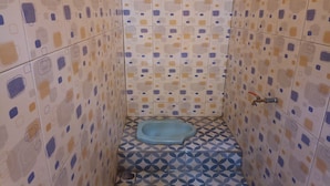 Une petite salle de bain avec des carreaux décorés, des toilettes bleues et un drain de douche.
