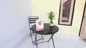 Un petit espace extérieur aménagé avec une table et des chaises, un pot de fleurs et un panneau posé sur la table.