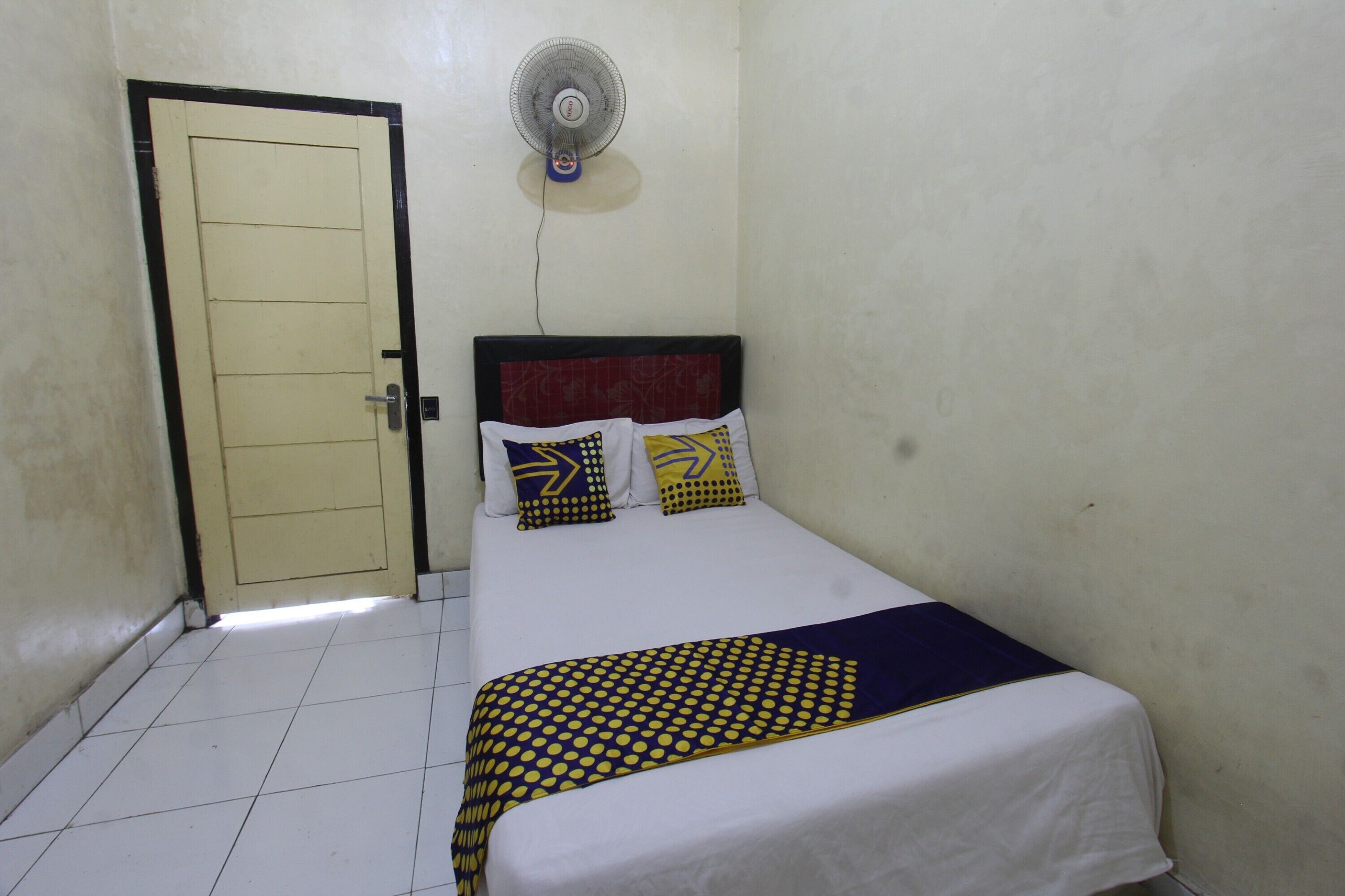 A bedroom with a bed, a door, and a wall-mounted fan.