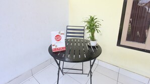 Une petite terrasse extérieure avec une table et une chaise en métal, un pot de fleurs et un panneau posé sur la table.