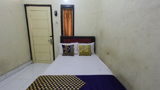 Un lit simple avec une couvre-lit à motifs, deux oreillers aux motifs géométriques, une porte et une fenêtre avec des rideaux.