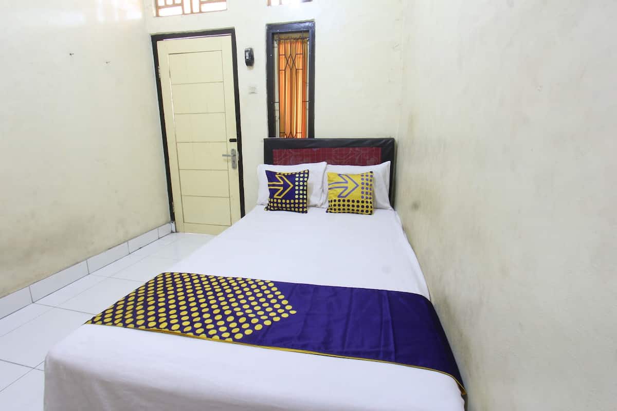 A single bed with a patterned bedspread, two pillows with geometric designs, a door, and a window with curtains.