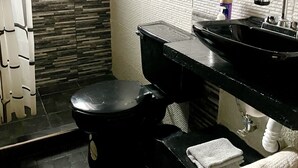 A bathroom with a black toilet, a black sink, and a mirror above the sink. There are towels on the floor and a bottle of soap on the sink. - House Green (Ecatepec de Morelos)