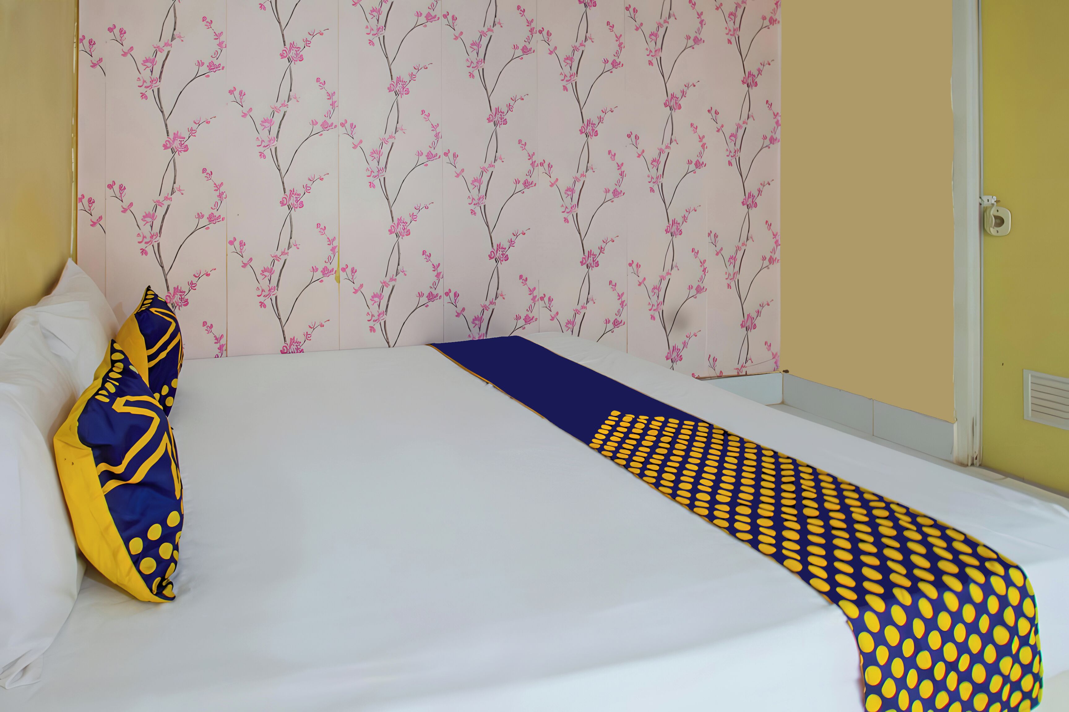 A neatly made bed with a white sheet and a blue and yellow patterned throw.