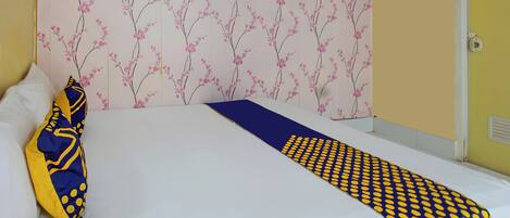Un letto rifatto con lenzuola bianche e una coperta decorata con motivi blu e gialli.