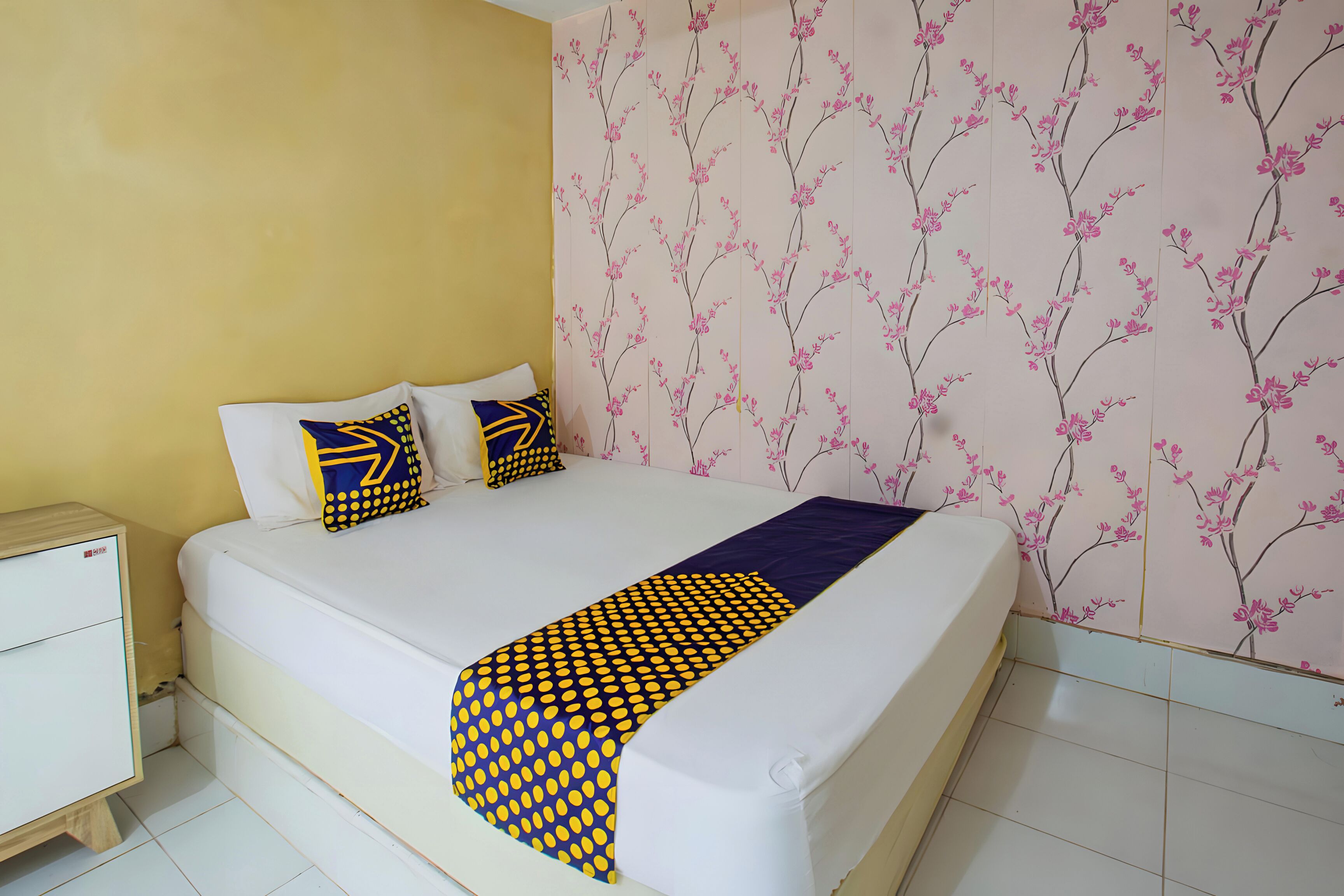 Een net opgemaakt bed met een geborreld kleed, twee kussens met geometrische patronen, en een nachtkastje met een lade.
