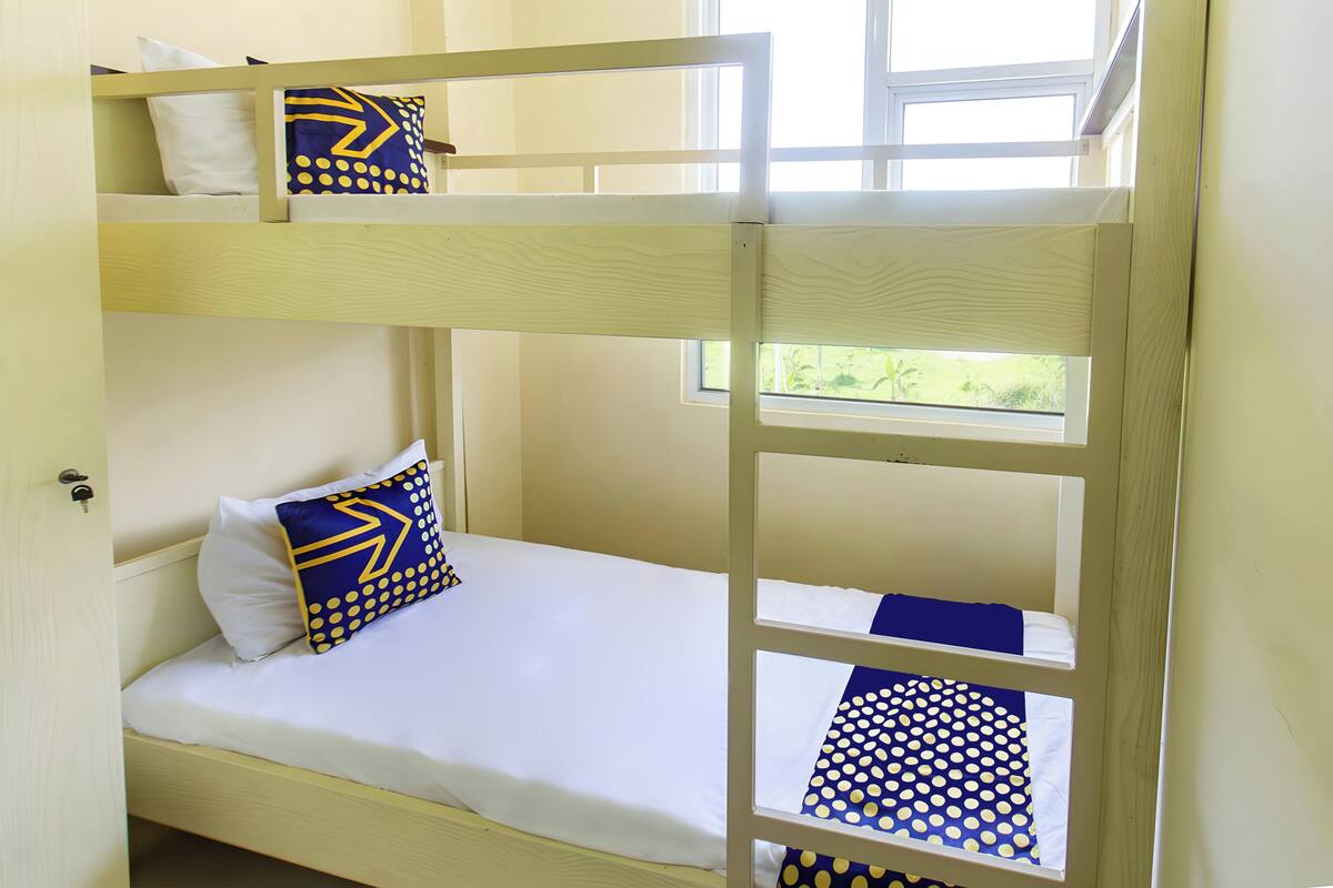 Een stapelbed met wit beddengoed en blauwe en gele kussens.
