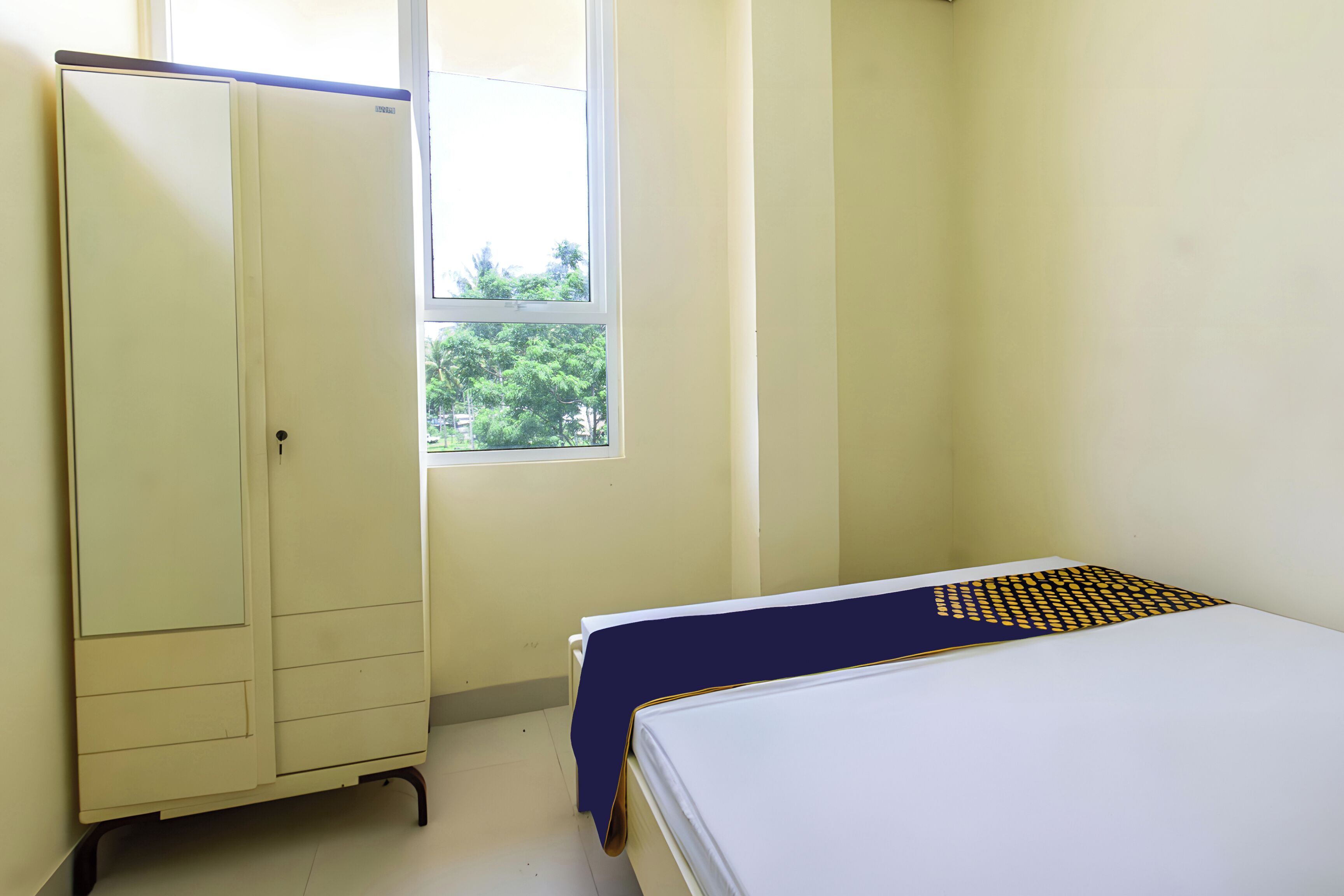 Una habitación con cama, armario y ventana con vistas a árboles.