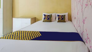 A bed with a white and blue bedspread, two pillows with yellow and blue patterns, and a wall with pink floral wallpaper. - OYO Life 93399 Kos Batulayar (Senggigi)