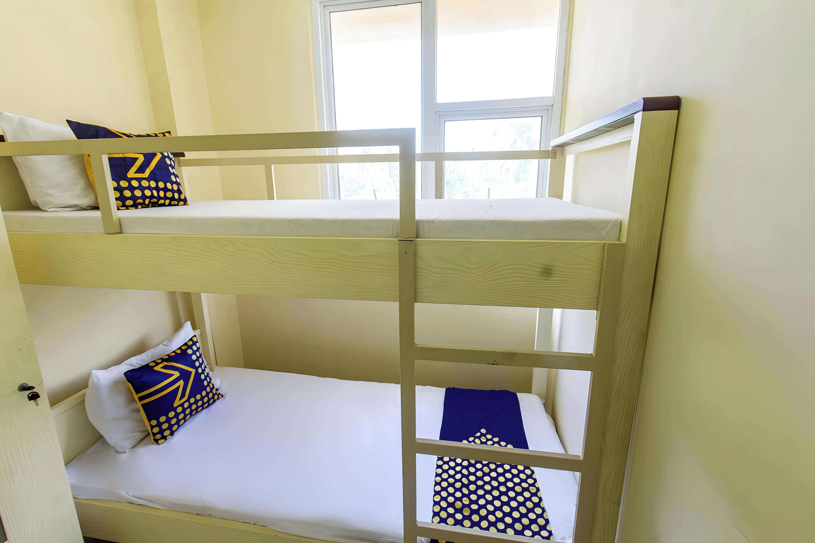 A bunk bed room with two levels, white bedding, and blue and yellow patterned pillows.