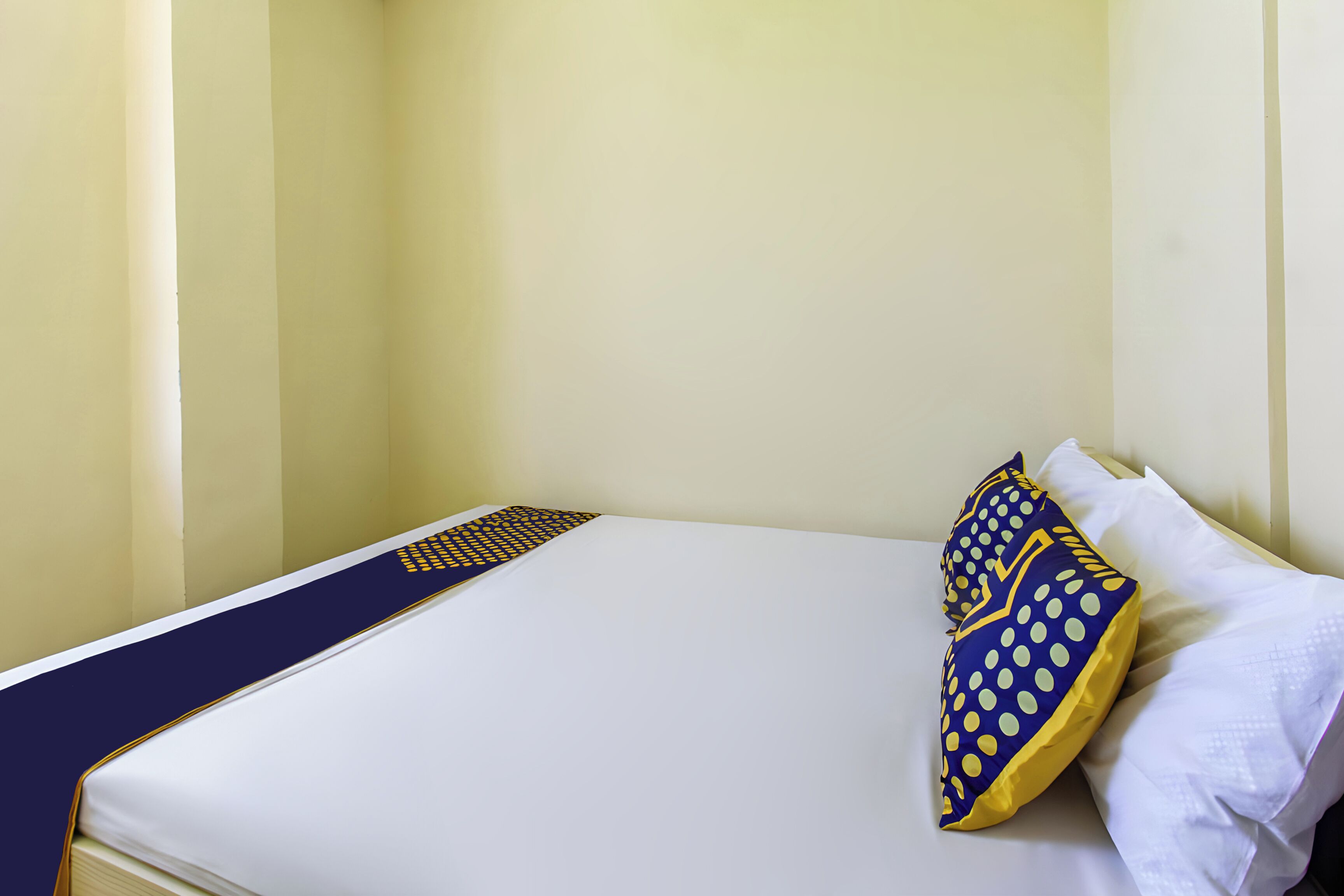 A neatly made bed with a white mattress and blue and yellow decorative pillows.