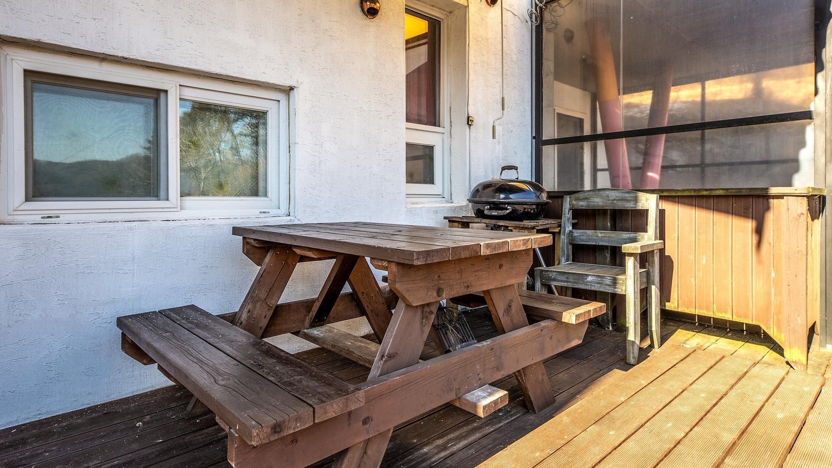 A wooden picnic table with benches, a grill, and a wooden fence.